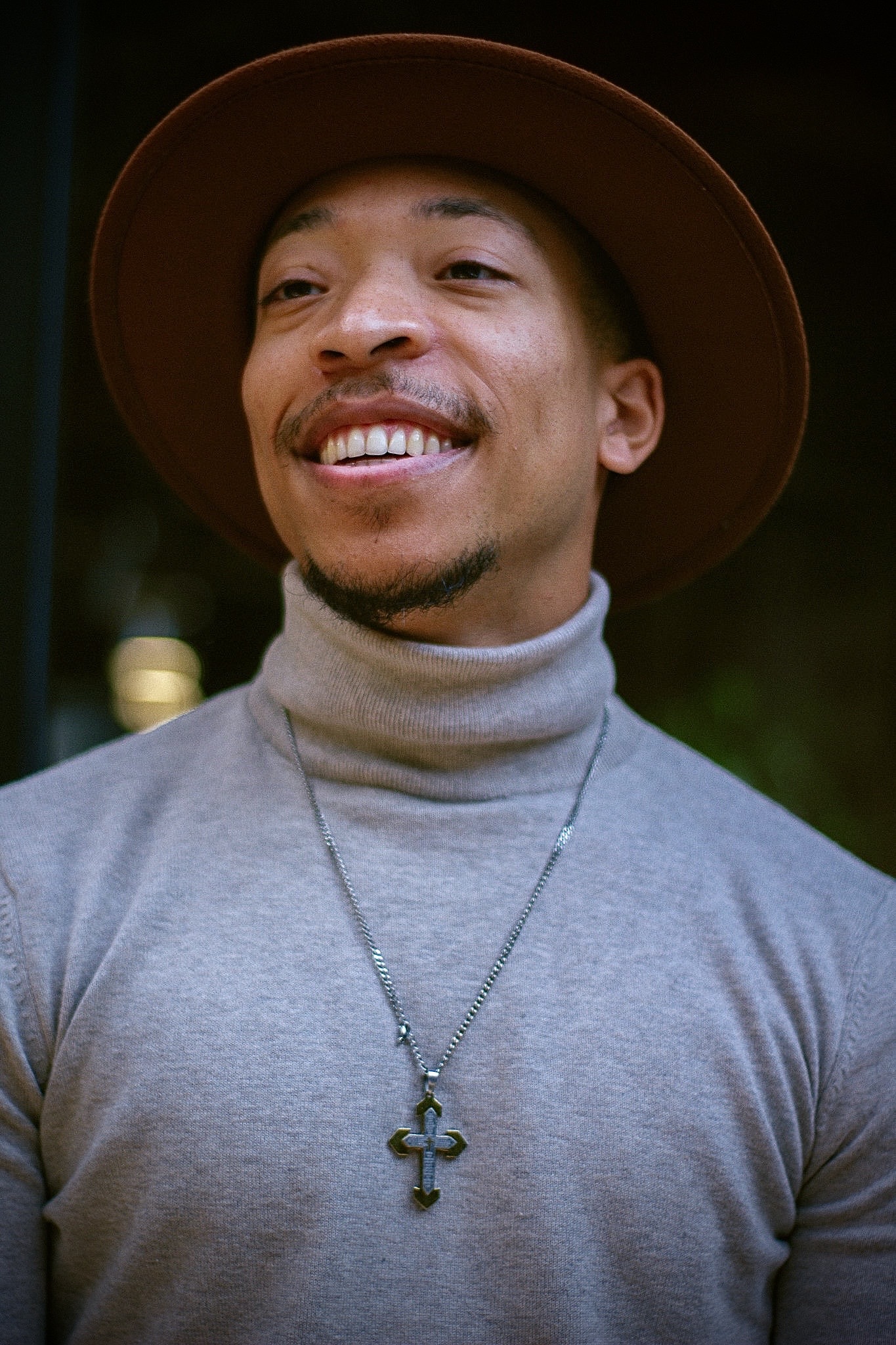 Cameron Bogans smiling in a brown hat and gray turtleneck